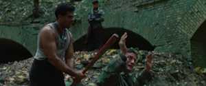 A Jew engaging in a cowardly homocide by bashing in a prisoner's skull with a baseball bat. He is enabled by multiple gunmen ready to fire.