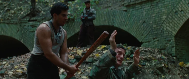 A Jew engaging in a cowardly homocide by bashing in a prisoner's skull with a baseball bat. He is enabled by multiple gunmen ready to fire.
